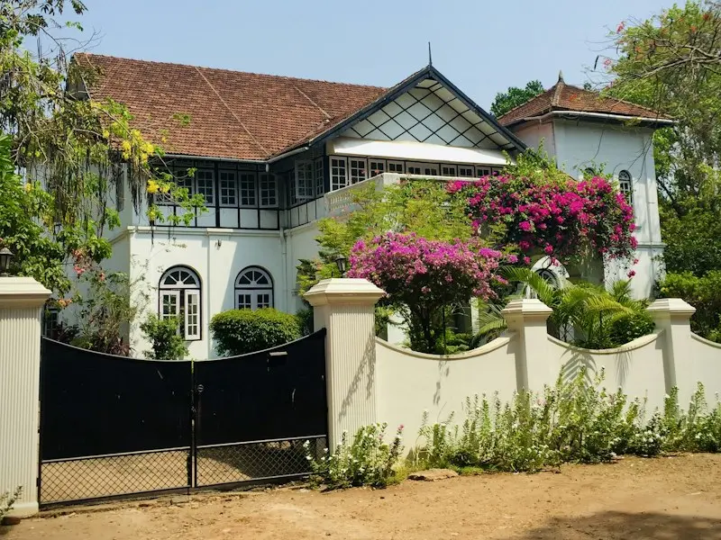 A whitewashed Kerala bungalow with a tiled roof behind a garden wall with bougainvillea